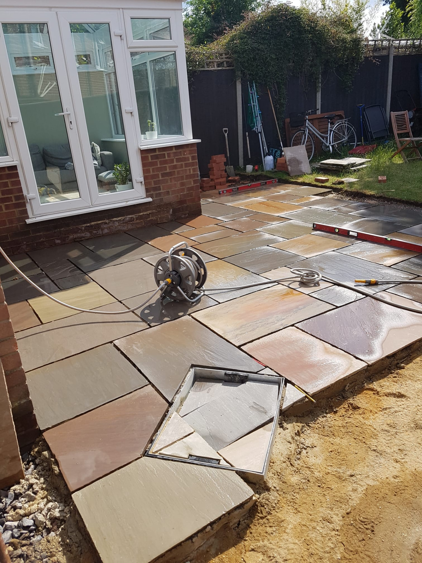 Sandstone patio being laid with brick edging outside a conservatory