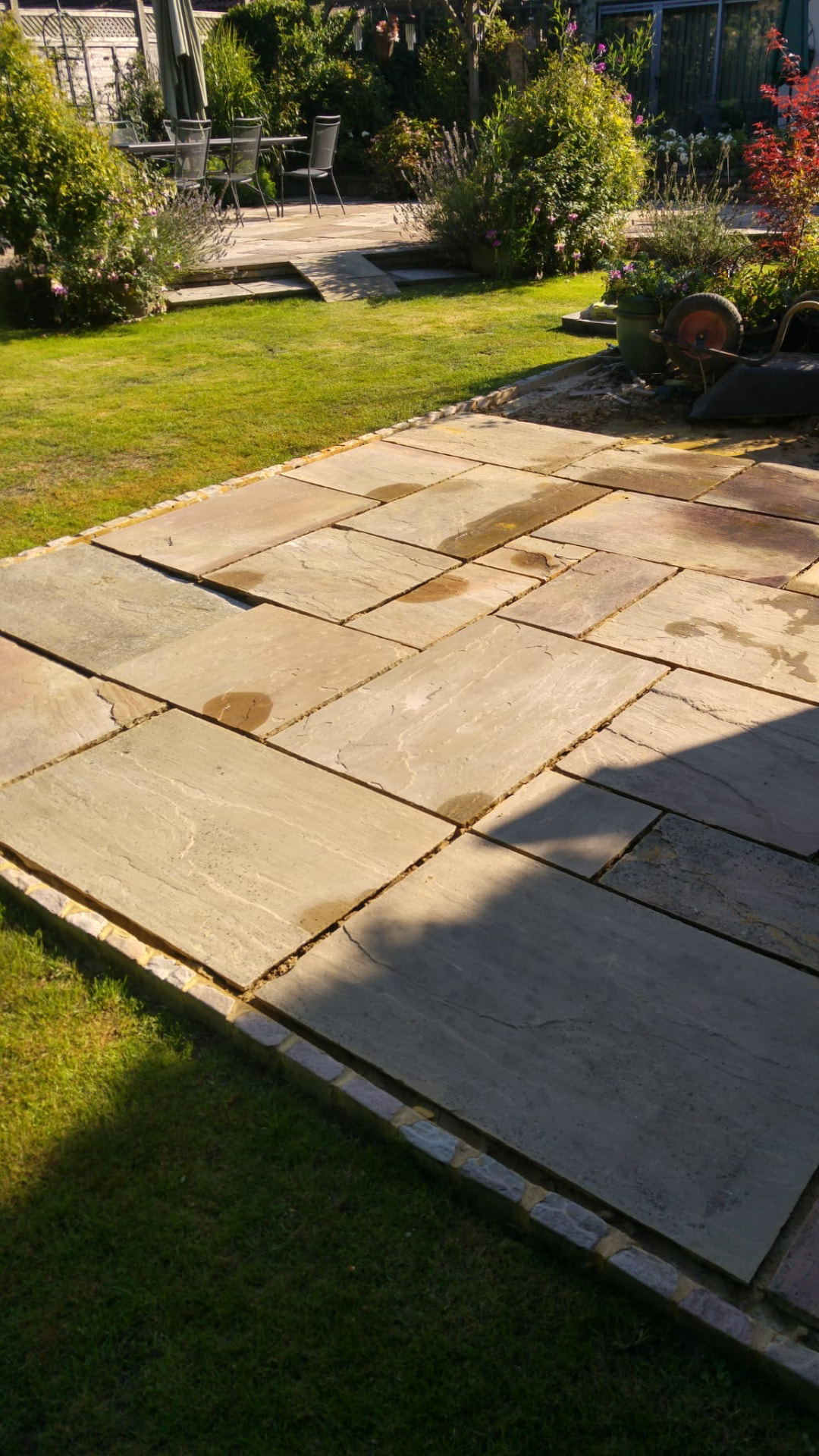 Large Indian sandstone patio with brick edging beside a manicured lawn at golden hour